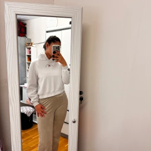 Vit hoodie Sunset Boulevard USA - Vit hoodie med tryck 'Sunset Boulevard U.S.A 1990' och amerikansk flagga på ryggen. Snygga ränder i blått och rött på ärmarna. Croppad passform och huva. Perfekt för chill dagar och streetstyle. Mjuk och skön i bomullsmix.