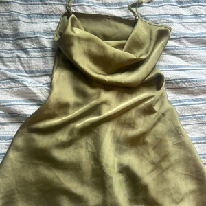 Olivgrön satinklänning med draperad hals - Säljer en olivgrön kortklänning i satin med smala axelband och snyggt draperad halsringning. Den är såå fin på och passar när man vill vara lite finare. Säljer bara för att den blivit lite förstor för mig, annars älskaar jag den💕