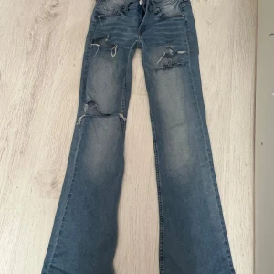 Bootcut jeans med slitningar, ljusblå - Ljusblå bootcut jeans med låg midja och snygga slitningar på låren och knäna. Jeansen har klassisk femficksdesign och är tillverkade i denim. Perfekta för dig som gillar en avslappnad och trendig look.