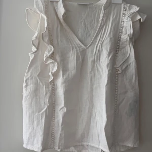 Vit volangblus från VILA, strl 34 - Supersöt vit blus från VILA med v-ringning och volangdetaljer längs axlarna. Storlek 34 men skulle säga att den även passar storlek 36. Nypris 399 kr. 