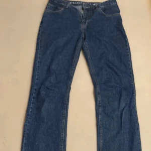 Blå jeans från Never Denim straight - Klassiska blå jeans från Never Denim med rak passform och normal midja. Jeansen har fem fickor, snygga kontrastsömmar och en brun läderpatch bak i midjan. Perfekta till sneakers eller boots för en chill look.