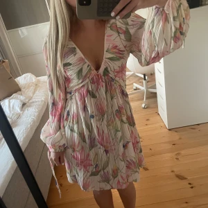 Blommig kortklänning med v-ringning - Superfin kortklänning med blommigt mönster. Klänningen har v-ringad hals, långa ärmar med knyt och plisserad struktur som ger en luftig känsla. Perfekt för sommarens alla tillfällen! Slutsåld💕