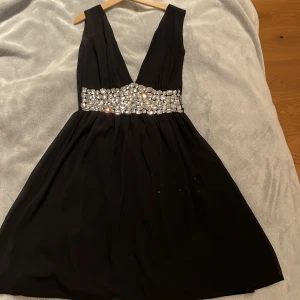 Svart kortklänning med strass från Club L - Supersnygg svart kortklänning från Club L med djup v-ringning och öppen rygg. Jag ÄLSKAR glittret på denna och skulle gärna ha den om det var så att den passade mig. Den är storlek 6 vilket motsvarar ungefär en Xs❤️