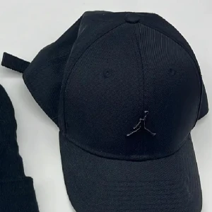 Svart keps från Jordan - Snygg svart keps från Jordan med den klassiska Jumpman-loggan framtill. Kepsen har böjd skärm och justerbar rem baktill för perfekt passform. Tillverkad i slitstark bomull, perfekt för en sportig och stilren look.