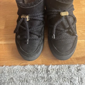 Svarta boots från Inuikii i mocka - Svarta boots från Inuikii med grova snören och snygga gulddetaljer. Skorna är i mjuk mocka och har en högre modell som passar perfekt till kalla dagar. Sulan är rejäl och ger bra grepp. Perfekta för dig som vill ha både stil och komfort.