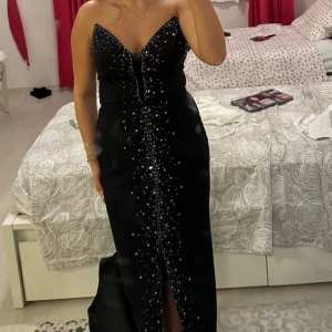 Bal/aftonklänning med stenar - Jättefin svart klänning men en slits och stenar framtill även en detalj vid brösten som inte syns på bilderna kan skicka  bilder om det önskas. Använd endast 1 gång storlek S/M. Kom gärna med prisförslag då jag kan tänka mig gå ner i pris!