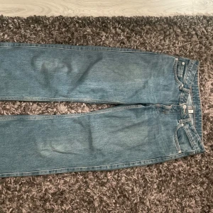 Blå jeans från weekday - Säljer ett par klassiska blå jeans från Arrow med raka ben och normal passform. Jeansen har fem fickor, silverfärgade nitar och kontrastsömmar. Materialet är slitstark denim i bomull och färgen är ljusblå med lätt tvättad look. Perfekt för dig som gillar enkel och tidlös stil.