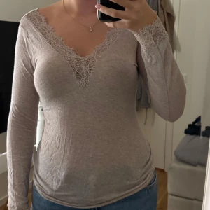 Beige långärmad topp med spets från intimissimi - Supersnygg beige långärmad topp med v-ringad hals och fina spetsdetaljer vid halsringning och ärmslut. Säljer då den inte används längre.