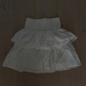 Vit volangkjol från KappAhl - Supersöt vit kortkjol från KappAhl med broderade små blommor och bred smock i midjan. Kjolen har dubbla volanger som ger en fluffig och lekfull look, perfekt för varma dagar. Tillverkad i mjuk bomull. Storlek 170 men passar mig som är vuxen S. Använd fåtal gånger tvättad 1 gång. Kan mötas på Ekerö annars står köparen för frakten 