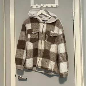 Rutig höst jacka - Mysig teddyjacka från SHEIN med stor rutig design i beige och vitt. Jackan har en vit huva, två bröstfickor med platta och runda knappar och dragkedja framtill. Perfekt för dig som gillar chill och comfy vibes under höst och vinter. Använd under en höst, har blivit lite ihoptuvad/lurvig.