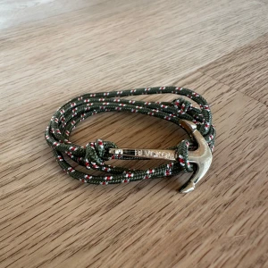 Grönt armband med ankare från Blvckout - Snyggt armband från Blvckout med grön, vit och röd flätad snodd och ett silvrigt ankare som lås. Perfekt accessoar för dig som gillar nautisk stil och detaljer som sticker gillar att sticka ut. Ny pris 399