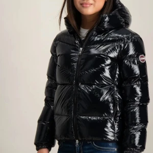 Svart glansig dunjacka från Colmar - Säljer min snygga svarta dunjacka från Colmar med glansig finish och vadderad design. Jackan har huva, dragkedja framtill och elastiska muddar vid ärmslut. Perfekt för kalla dagar när du vill hålla stilen och värmen🍂