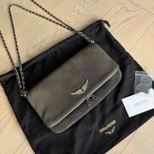 Zadig väska - Nu säljer jag min limiterade gråa mockaväska från Zadig & Voltaire med silverfärgad kedjerem. Väskan går att bära på många olika sätt då det finns två kedjor i olika längder som är avtagbara. Den är väl omhändertagen och har inga skador eller repor. Kommer med dustbag och extra tag.💓