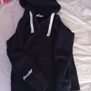 Svart hoodie med dragkedja russemerch - Marinblå hoodie från Russemerch i storlek S. Tröjan har vit snörning i huvan, hel dragkedja framtill och broderad logga på ärmen. Mjuk insida och klassisk passform, perfekt för chill dagar. Snygg och enkel att matcha med jeans eller joggers. Pris kan diskuteras 