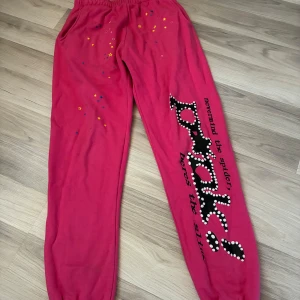 Rosa mjukisbyxor med stjärnor och tryck - Rosa mjukisbyxor med resår i midjan och benslut. Byxorna har färgglada stjärnor upptill och ett stort tryck längs ena benet med text och prickar. Perfekta för chill dagar eller när du vill sticka ut lite extra.