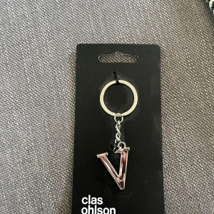 Nyckelring med bokstav V från Clas Ohlson - Snygg nyckelring i metall med en glansig bokstav V i silverfärg. Perfekt att hänga på väskan eller nyckelknippan för en personlig touch. Kommer på originalförpackning.
