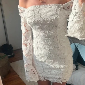 Vit spetsklänning med lång ärm - Superfin vit kort spetsklänning med långärmade ärmar och v-ringad rygg. Klänningen har blommigt spetsmönster och sitter tajt men bekvämt. Perfekt för dig som vill sticka ut med en romantisk och elegant look.