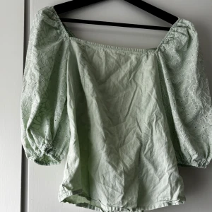 Ljusgrön/mintgrön blus - Blusen har kort puffärm med vackert broderat spetsmönster och små hålbroderier, vilket ger en feminin och luftig känsla. Rak passform med fyrkantig urringning framtill. Perfekt till sommaren, både till vardags eller festligare tillfällen. Den kan kännas lite som oversize