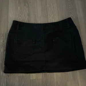 Svart jeanskjol med fickor - Snygg svart kort jeanskjol med klassisk femficksdesign och bälteshällor. Kjolen har raka linjer och stängs med knapp och dragkedja framtill. Perfekt att matcha med en cool t-shirt eller hoodie för en avslappnad look.