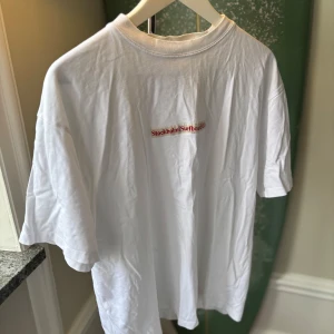 Vit t-shirt Stockholm Surfboard Club - Vit t-shirt från Stockholm (Surfboard) Club i 100% ekologisk bomull. Klassisk passform med korta ärmar och rund hals. Diskret röd logga tryckt på bröstet. Perfekt basic-plagg med clean vibe.