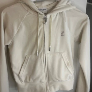 Vit Juicy Couture zip hoodie  - Superfin vit hoodie från Juicy Couture i mjuk velour med huva och dragkedja. Stora strasstenar bildar texten 'Juicy' på ryggen och ett litet JC-märke framtill. Klassisk känguruficka och snygga detaljer på snörningen. Tar emot pris förslag💕