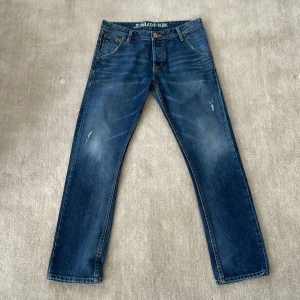 Blå Tom Tailor jeans med slitningar - Snygga blå jeans straight fit med coola slitningar och detaljer på både fram- och bakfickor. Klassisk femficksmodell med läderpatch bak. Sjukt snygga och passar till mycket. Passar större än w30 då jag själv är w32 och dom passar mig