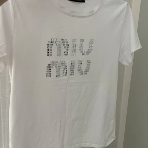Vit Miu Miu t-shirt med silverdetaljer - Vit t-shirt från Miu Miu med korta ärmar och rund hals. Framsidan har coola silvriga detaljer som bildar Miu Miu-loggan i ett rutigt mönster.