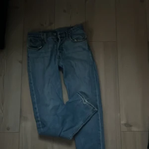 Levi's 501 ljusblå jeans - Klassiska Levi's 501 jeans i ljusblå denim. Rak passform med fem fickor och knappgylf. Ikonisk röd Levi's-tag på bakfickan. Perfekta för dig som gillar tidlös och avslappnad stil.