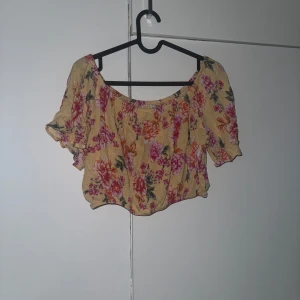 Gul blommig croppad topp - Superfin gul croppad topp med blommigt mönster i rosa och rött. Perfekt för varma dagar och ger en romantisk vibe till outfiten. Storlek S.
