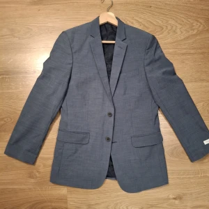 Blå kavaj från Calvin Klein - Snygg blå kavaj från Calvin Klein med två knappar framtill, klassisk krage och flera fickor. Fodret är svart med diskret logga invävd. Perfekt för dig som vill ha en stilren och modern look.