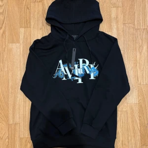 Svart hoodie från Amiri med draktryck - Svart hoodie från Amiri med stor logga och blå drake tryckt över bröstet. Tröjan har huva med snörning. Riktigt fet och har extremt bra kvalite. Skriv om du har några frågor:)