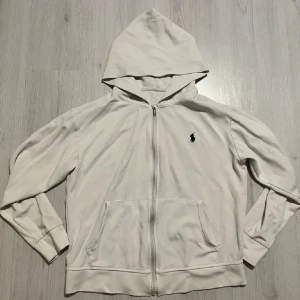Vit zip hoodie från Ralph Lauren - Vit hoodie från Ralph Lauren med dragkedja framtill och klassisk svart logga på bröstet. Är i storlek S men har krympt i tvätten så passar mer en Xs. Pris är ej hugget i sten 🤩🙌