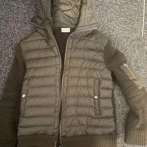 Moncler grön cardigan jacka med huva - Snygg grön cardigan jacka från Moncler med stickade ärmar och quiltad front. Jackan har huva, dragkedja och två fickor framtill. Moncler-logga på ärmen och cool detaljficka med dragkedja. Perfekt för dig som vill ha en stilren och bekväm look. Storlek på jackan är S och sitter bra på mig som är 175cm lång nypris på jackan var 12800kr och säljs för mer än 50% av perfekt jacka nu för hösten och impar väldigt på folk Pris är ej hugget i sten skriv om du undrar något.