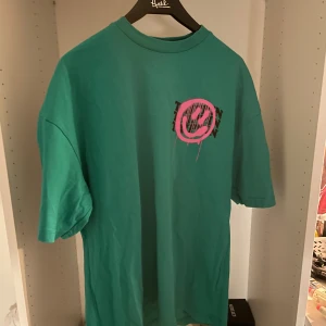 Turkos oversized t-shirt från FSBN - Turkos oversized t-shirt från FSBN med coolt tryck av en stor rosa smiley och texten 'TRIPPIN' i svart. T-shirten har korta ärmar och är gjord i mjuk bomull. Perfekt för dig som gillar streetstyle och vill sticka ut med färg och grafiskt tryck. Aldrig använd