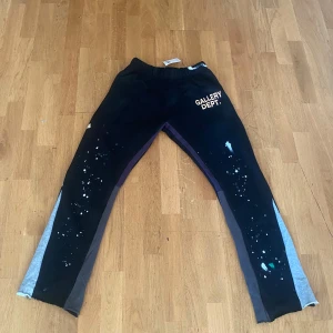 Gallery Dept mjukisbyxor - Sköna och snygga med elastisk midja och flared ben. Grå/mörkblå paneler på sidorna, vitt tryck på ena benet och färgstänk i vitt och blått fram. Gjorda i 100% bomull – perfekt för streetwear och avslappnat häng. Pris kan diskuteras, hör av dig