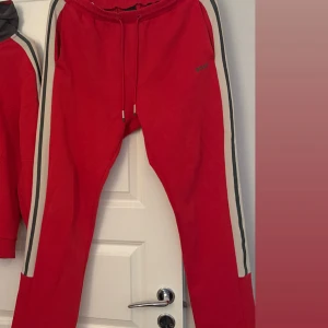 Röda mjukisbyxor från BOSS - Riktigt snygga röda mjukisbyxor från BOSS med vita och svarta ränder längs sidorna. Byxorna har snörning i midjan och diskret BOSS-logga på ena benet. Perfekta för en chill och sportig look.