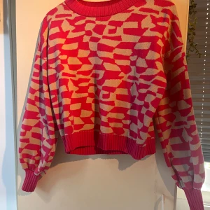 Rosa och beige stickad tröja från Cider - Cool stickad tröja från Cider i rosa och beige med unikt spräckligt mönster. Tröjan har ribbade muddar och rund hals, samt ballongärmar. Perfekt för dig som vill sticka ut med färg och mönster. Färgerna är mer kalla irl.  Frakt tillkommer