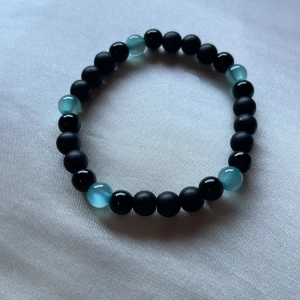 Svart och blått pärlarmband - Stilrent armband med svarta och ljusblå pärlor på elastisk tråd. De svarta pärlorna är matta medan de blå är glansiga och ger en snygg kontrast. Perfekt accessoar för att lyfta din outfit med en cool och enkel vibe.