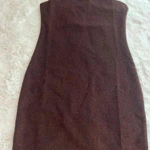Brun glittrig tubklänning H&M Divided - Snygg brun tubklänning från H&M Divided i storlek S. Klänningen är kort och har ett glittrigt tyg som ger en festlig känsla. Tight passform som framhäver figuren och är perfekt för dig som gillar att sticka ut.