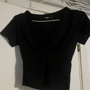 Svart v-ringad topp från BikBok XS - Svart kortärmad topp från BikBok i storlek XS. Toppen har en snygg v-ringning och figurnära passform som framhäver siluetten. Perfekt att matcha med jeans eller kjol för en stilren look.