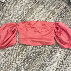 Rosa offshoulder topp från Bik Bok - Säljer en snygg rosa offshoulder topp från Bik Bok i satinliknande material. Toppen har voluminösa puffärmar och dragkedja bak 
