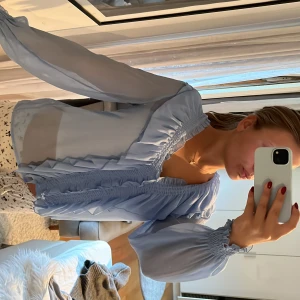 Ljusblå volangblus från Zara - Supersöt ljusblå blus från Zara med volangdetaljer längs v-ringningen och framtill. Blusen är i ett tunt, transparent tyg med långa ärmar och smock vid ärmslut. Perfekt för dig som gillar romantiska vibes och flowy look.