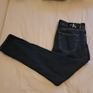 Blå jeans från Calvin Klein Jeans W31 L32 - Säljer ett par klassiska blå jeans från Calvin Klein Jeans i rak modell. Jeansen har fem fickor, snygga kontrastsömmar och ikonisk CK-lapp bak i midjan. Tillverkade i slitstarkt bomullsjeansmaterial. Perfekta för en clean och tidlös look. Köpt för 800