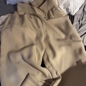 Beiga vida byxor med resårmidja - Snygga beiga byxor med bred resår i midjan och avslappnad, vid passform. Tillverkade i ett mjukt och lätt tyg som ger en skön känsla. Perfekta för en chill, sommar och stilren look.