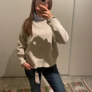 Beige stickad polotröja - Mysig beige stickad polotröja med hög krage och avslappnad passform. 