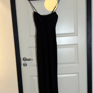 Svart långklänning från Gina Tricot - Supersnygg svart långklänning från Gina Tricot med smala axelband och lätt rynkad byst. Klänningen har en enkel och stilren design med knyt fram och figurnära passform. Perfekt för dig som vill ha en klassisk look med en modern twist. Klänningen är siden ! 