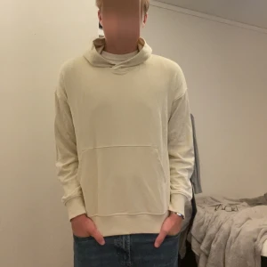 Beige hoodie med huva - Säljer en stilren beige hoodie med huva och känguruficka framtill. Tröjan har en avslappnad passform och är perfekt för chill dagar. Långa ärmar och mjukt material gör den extra skön att bära. 