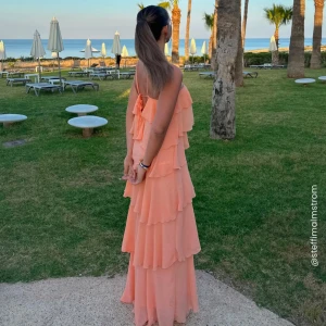 Persikofärgad volangklänning med knyt - Jättefin volang klänning som endast är använd vid ett tillfälle, så är som ny. Storlek L men passar mig som vanligtvis har S och M, köpte större då jag är 173cm och ville ha den lång. 