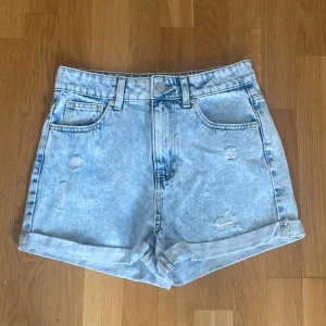 Ljusblå jeansshorts från FB Sister - Ljusblå, högmidjade jeansshorts från FB Sister med upprullade benslut och slitna detaljer framtill och på bakfickorna. Klassisk femficksmodell i denim med bälteshällor och knappstängning. Storlek S Perfekta för sommaren!