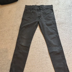 Svarta Replay jeans slim fit 32/32 - Snygga svarta jeans från Replay i modellen slim fit. Klassisk femficksdesign, raka ben och diskreta detaljer på bakfickorna. Jeansen är tillverkade i ett mjukt bomullsmaterial med lite stretch för extra komfort. Perfekta för en clean och stilren look.